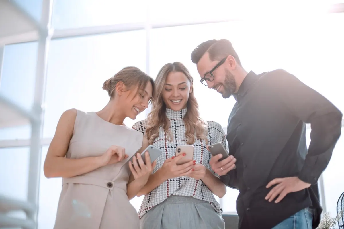 Three colleagues look at a phone together in a bright office