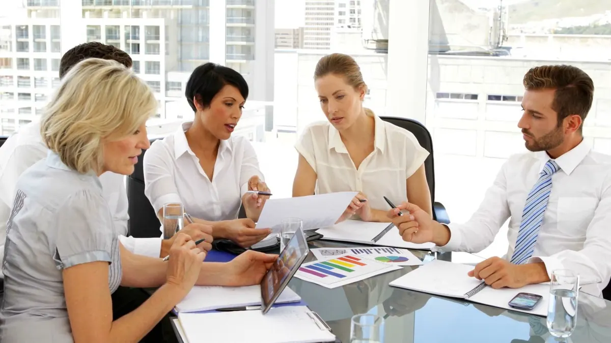 Five colleagues discuss charts around a meeting table in a bright office